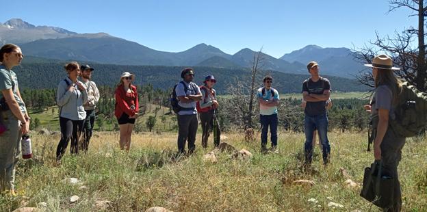Eight students standing in front of a mountain range talking to a park ranger.